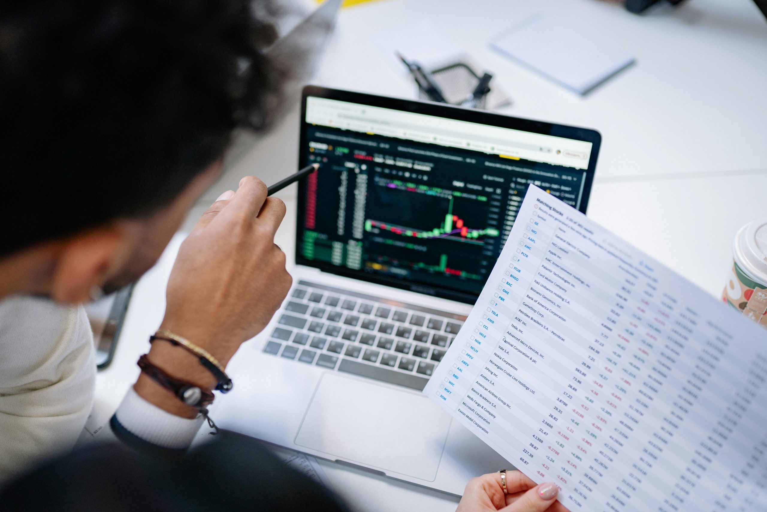 A person is pointing at a laptop screen with charts and graphs on it.