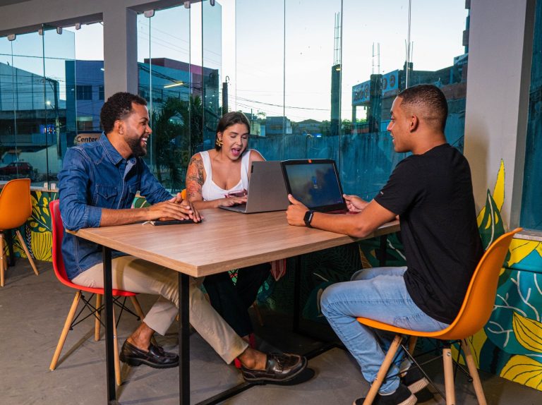 Three colleagues sitting at a table working on laptops in a vibrant, urban office space.