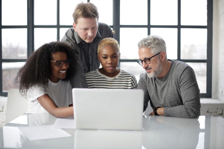 A diverse team of adults collaborating over a laptop in a bright, modern office.