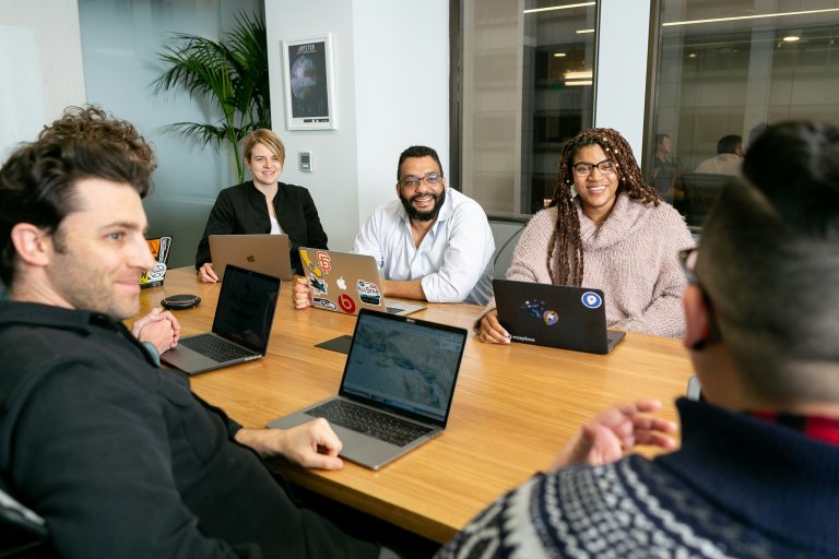 A table of people smiling with their laptops opened in front of them