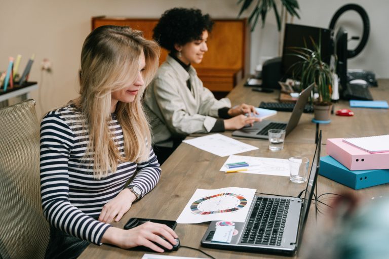 A desk with two people working on their laptops